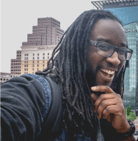a headshot of a men with a long braided hair and black glasses